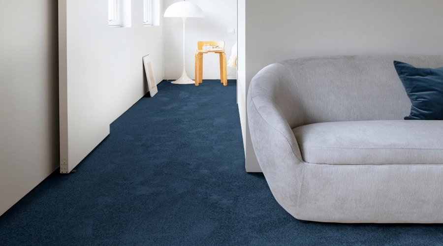 Deep blue loop pile wall to wall carpet alongside a grey couch